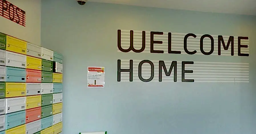 Entrance saying 'Welcome Home' and multi-coloured locked post boxes